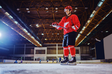 Attractive caucasian hockey player standing on ice and removing ice from stick. Hall interior....
