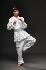 a teenager dressed in martial arts clothing poses on a dark gray background, a sports concept