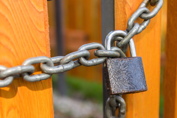 A padlock on a steel chain hangs and locks the doors of a yellow new wooden fence