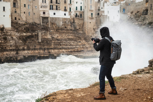 Photographer taking picture of a stormy sea in Polignano a Mare, Italy