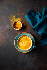 Top down view of turmeric latte cup on a textured dark background.