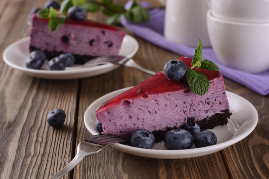 Pair of slices of blueberry mousse cake with mirror glaze decorated berries and leaves of mint for delicious enjoyment