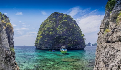 view of a ship floating in blue-green sea with small island and blue sky background, Maya bay, Phi Phi islands, Krabi, southern of Thailand.