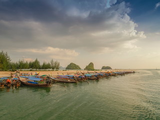Fototapeta na wymiar sea view evening of many long-tail boats floating seaside with green trees and cloudy sky background, Ao Nang Pier, Krabi, southern of Thailand.