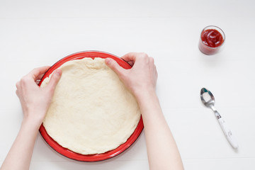 The process of cooking pizza at the stage of rolling out the dough and spread with ketchup, on a white background. The concept of making pizza.