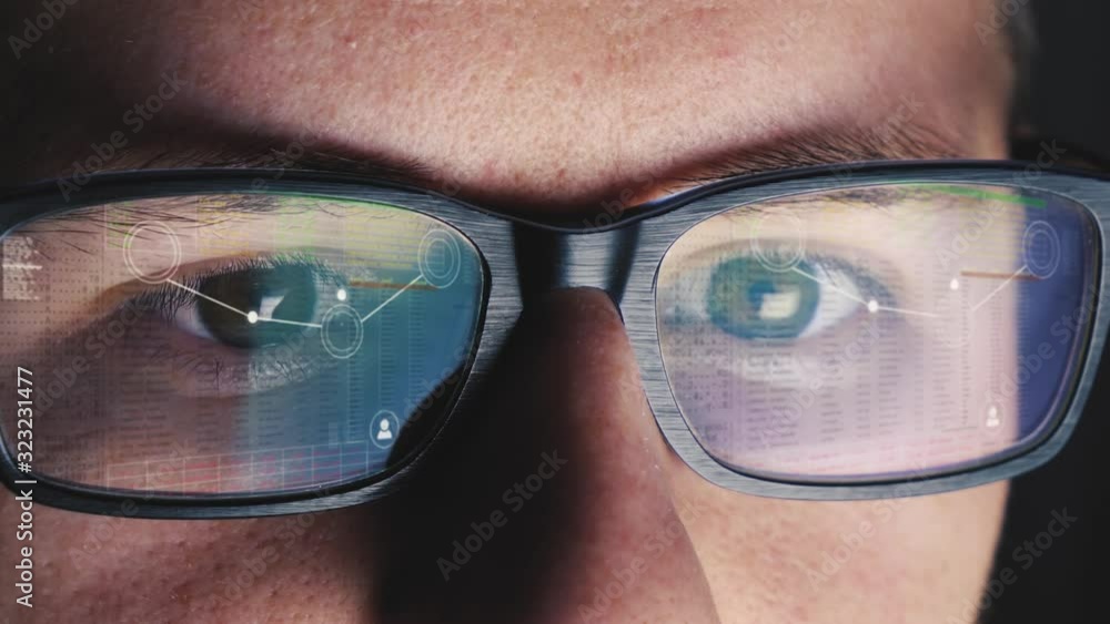 Poster man leans over to his computer screen and begins to code - image is reflected on his glasses