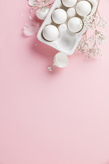 White eggs  in white ceramic holder and flowers on pink background