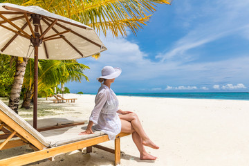 Beautiful woman white beach dress sitting on sunbed lounges watching the calm sea. Tropical...