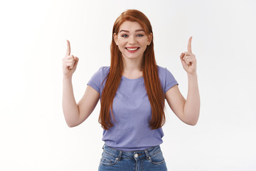 Excited, happy overwhelmed good-looking redhead woman in purple t-shirt, pointing fingers up, smiling joyfully, overjoy from amazement, inform about stunning great offer, white background