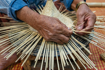 Hands of old artisan craftsman elderly working weaving rattan and bamboo to make ancient handmade...