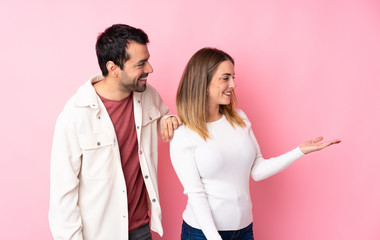 Couple in Valentine Day over isolated pink background pointing back and presenting a product