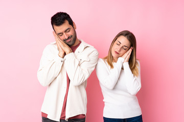 Couple in Valentine Day over isolated pink background making sleep gesture in dorable expression