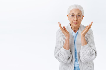 Oh dear grandmother looking at child grown up so fast, raising hands near cheeks from cuteness and lovely scene, being touched and impressed, smiling happily, standing white background in glasses