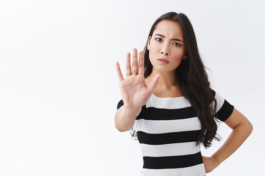 Time to slow down and stop. Serious-looking angry young confident woman pull hand forward and staring camera troubled, forbid something, make prohibition gesture, stand white background