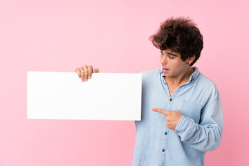 Young caucasian man over isolated pink background holding an empty white placard for insert a concept