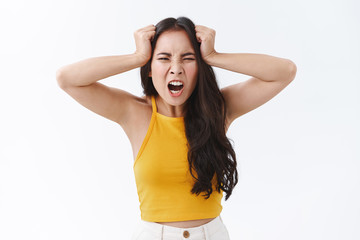 Hateful and outraged, pissed east-asian furious woman cursing someone and swearing as feeling betrayed or cheated on, holding hands on head distressed, frowning with angry grimace, white background