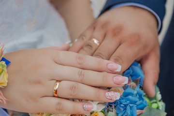 Beautiful hands with wedding rings of the newlyweds on a bouquet.