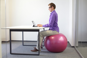 man on stability ball working with tablet - correct sitting position at the desk