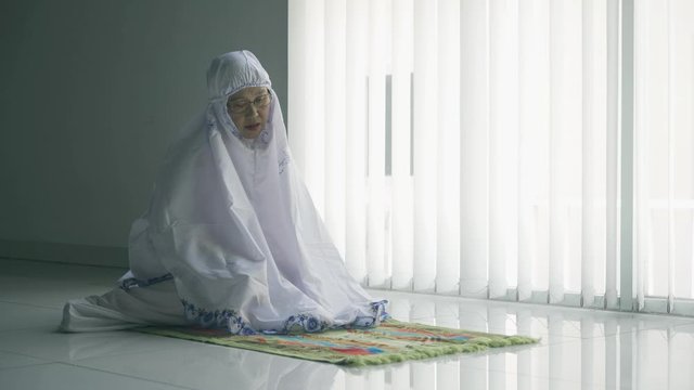 Senior Muslim woman praying alone near the window