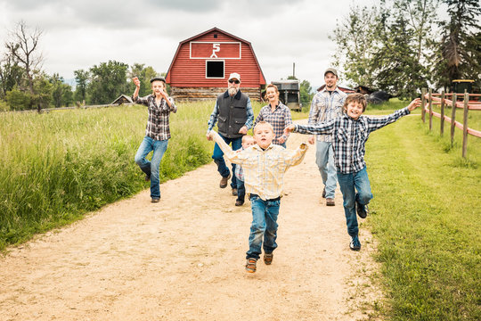 Western family running together down driveway with barn in background. Red Lodge, Montana, USA