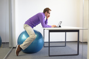 Man on stability ball working with tablet at desk in the office - changing siting  position
