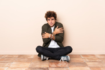 Young caucasian man sitting on the floor freezing