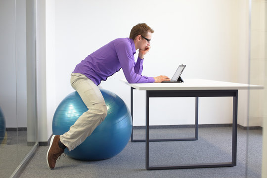 Man on stability ball working with tablet at desk in the office - changing siting  position