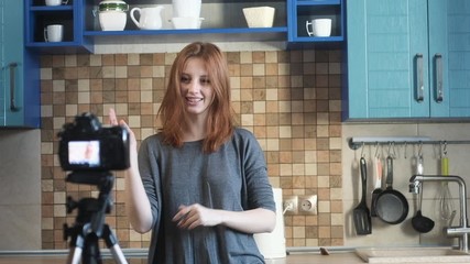 blogger girl records video blog in kitchen. woman removes vlog and actively waving hands talking to camera. attractive girl shoots an online vlog for followers and likes on camera. Online broadcast.