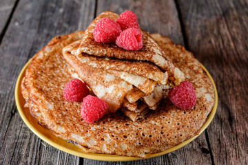 On a table made of old gray boards, there is a tall stack of delicious freshly baked homemade pancakes on a plate. Pancakes are served with raspberries.  Celebration Of Russian Maslenitsa.