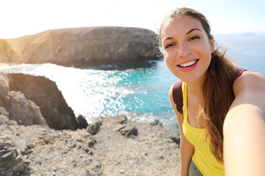 Tourist woman taking selfie picture at Playa Papagayo landscape. Happy beautiful girl take self portrait of Lanzarote landscape with Playa Papagayo beach in Canary Islands, Spain.