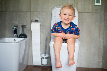 Happy little baby boy sitting on toilet and training to urinate and defecate into