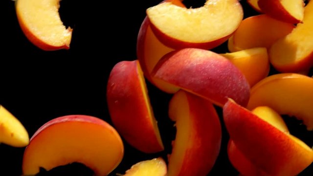 Juicy peach slices are flying diagonally on the black background in slow motion