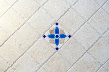 Beautiful beige tiles with uneven edges are laid out diagonally. Background. In the center is a tile with a blue floral pattern