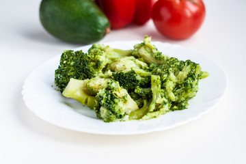 Plate with boiled broccoli, in the background vegetables red sweet pepper, tomato and avocado