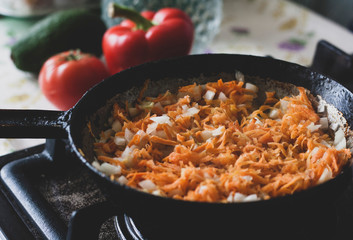 Roasting carrots and onions in an old cast-iron skillet on the stove in the kitchen