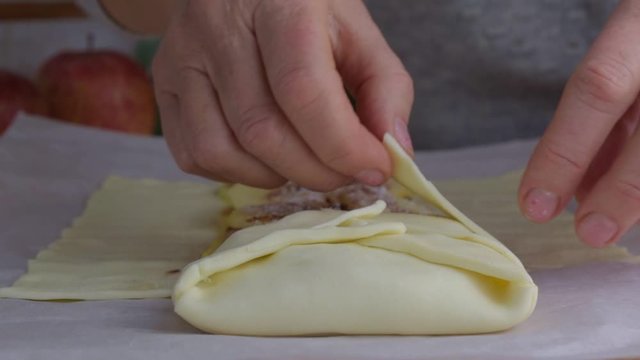mature woman hands make delicious strudel with apples from rolled dough on table with parchment in kitchen close view