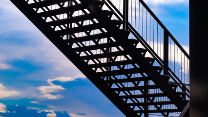 side view of outside metal staircase or fire exit stair with sheet  against blue sky. moving up concept idea