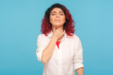 Colds and flu epidemic. Portrait of unhealthy woman with fancy red hair touching neck, suffering sore throat, feeling pain in tonsils, hard to swallow. indoor studio shot isolated on blue background