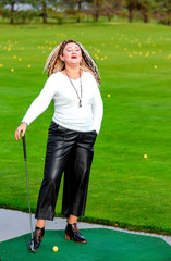 Laughing girl with curly hair and a club in her hands on a golf course with yellow balls in Riga, Latvia. Concept - healthy lifestyle.