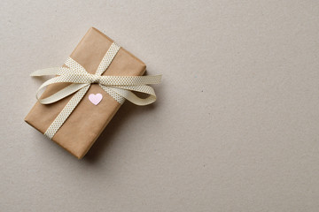 Handmade gift box with a heart, tied with a beige ribbon with a bow, on a cardboard box with space for text.