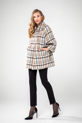 cute blonde model posing in brown striped white coat. white background. standing. studio shot.