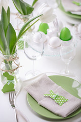 Decor and table setting of the Easter table with white tulips and dishes of green and white color. Easter decor in the form of Easter bunnies  green color with white polka dots.