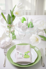 Decor and table setting of the Easter table with white tulips and dishes of green and white color. Easter decor in the form of Easter bunnies  green color with white polka dots.