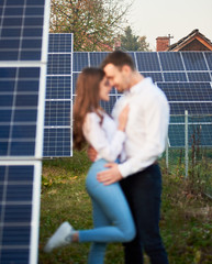 Focus on the background of a row of solar panels on a plantation near the house. Defocused couple...