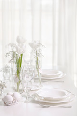Happy Easter! Decor and table setting of the Easter table with white tulips and dishes of white color.