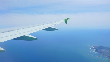 View from the airplane porthole. Landscape: sky, sea, island, airplane wing