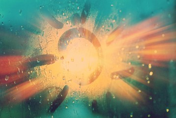 The sun is painted on a foggy window. Raindrops on the glass. Blue background.
