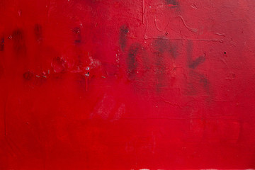 metal surface painted with red paint with streaks and barely distinguishable inscription work. Red grunge background.