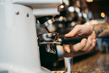 Close up shot of professional bartender preparing espresso coffee in exclusive cafe bar or cafeteria. He using coffee mill or grinder.