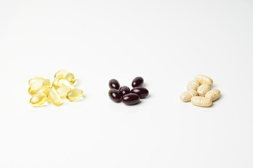 Three bunches of multivitamins, fish oil and astaxanthin. Keto-carotenoid in the middle. White background. Close-up.